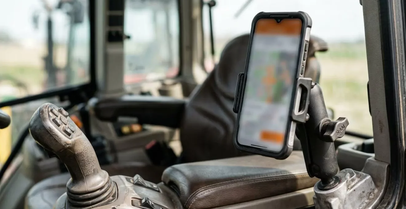 Smartphone mit landwirtschaftlicher Flottenmanagement-App in moderner Traktorkabine montiert